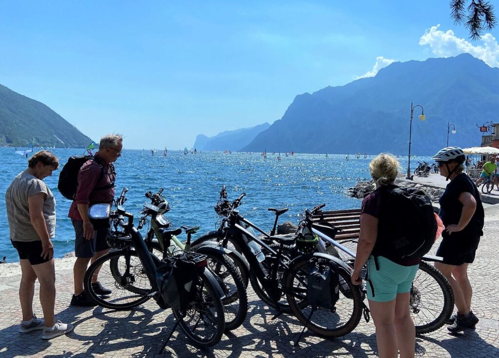 Gruppe Fahrradfahrer am Ende der Tour stehen am Ufer des Gardasees an der Promenade von Torbole