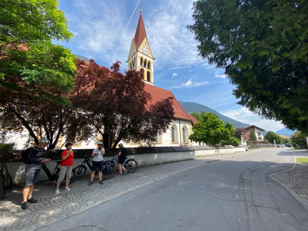 Radfahrer im Schatten eines Baumes vor malerischer Kirche