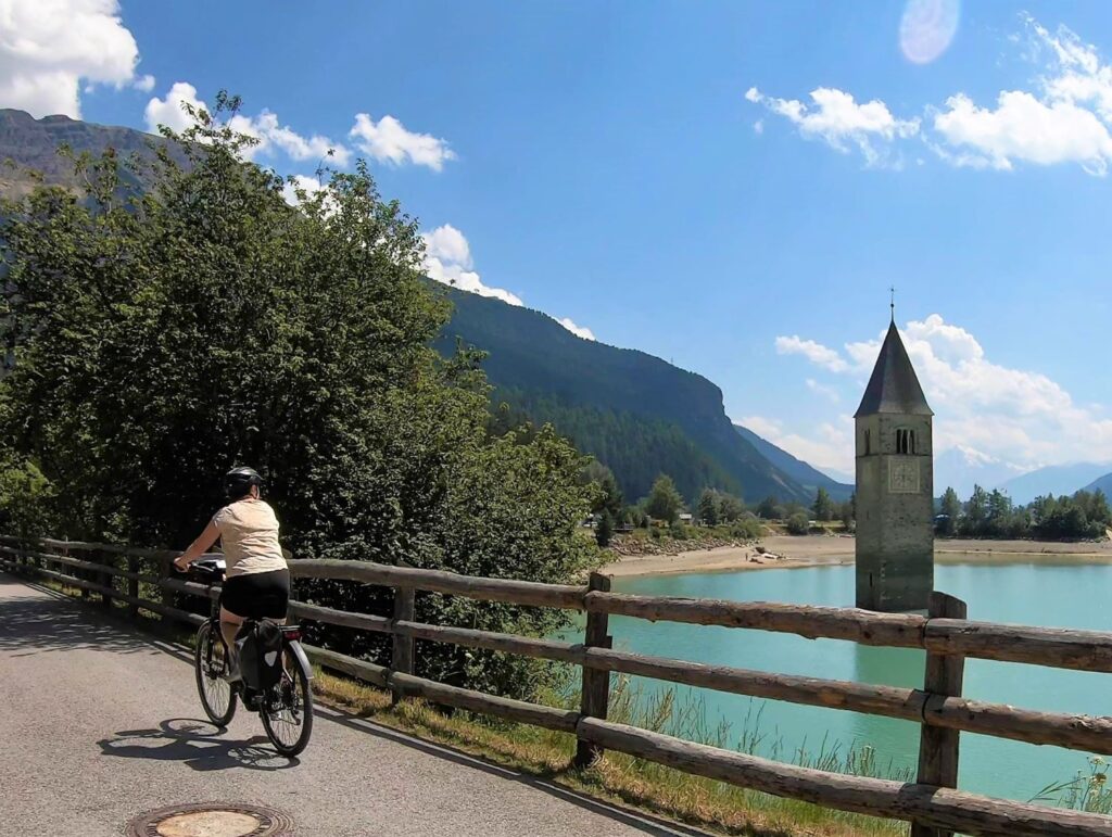 Kirchturm von Graun im Reschensee mit Radfahrerin